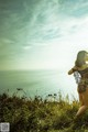 A woman in a black lingerie standing on a grassy hill overlooking the ocean.