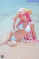 A woman in a bikini and hat sitting on the beach.