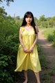 A woman in a yellow dress standing on a dirt road.