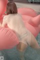 A woman in a white bodysuit sitting on an inflatable flamingo in a pool.